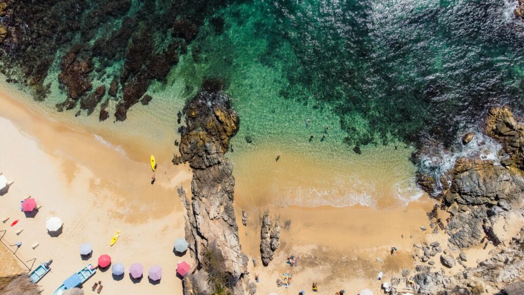 Drone shot of Estacahuite Beach, showcasing vibrant waters and beach activities. Perfect for summer travel.