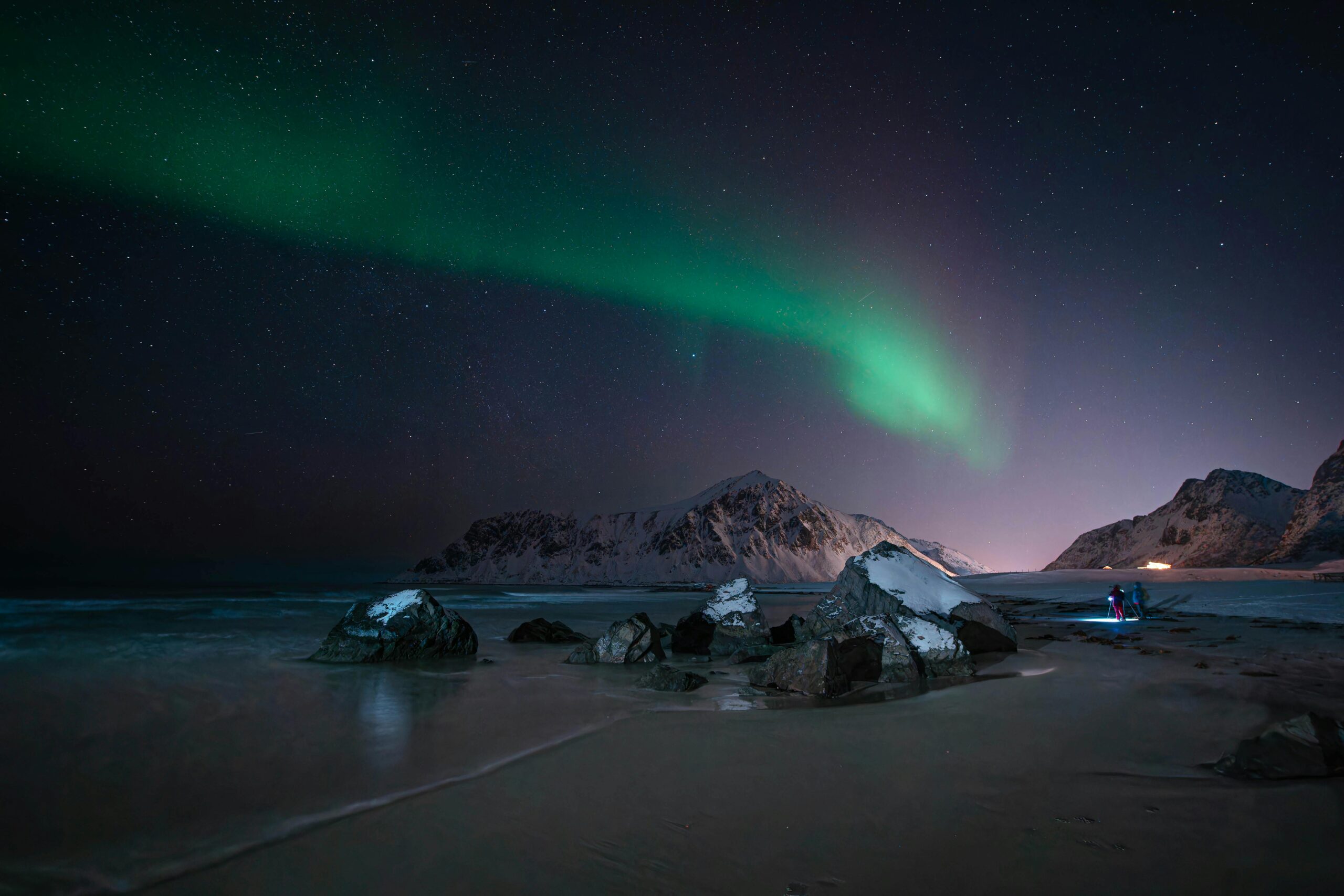 Captivating night view of aurora borealis over rocky Flakstad beach with stars illuminating the sky.