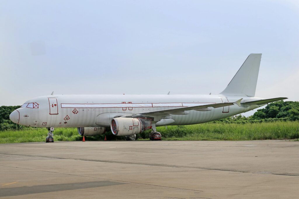 A white commercial airplane parked on a runway by lush green countryside during summer.