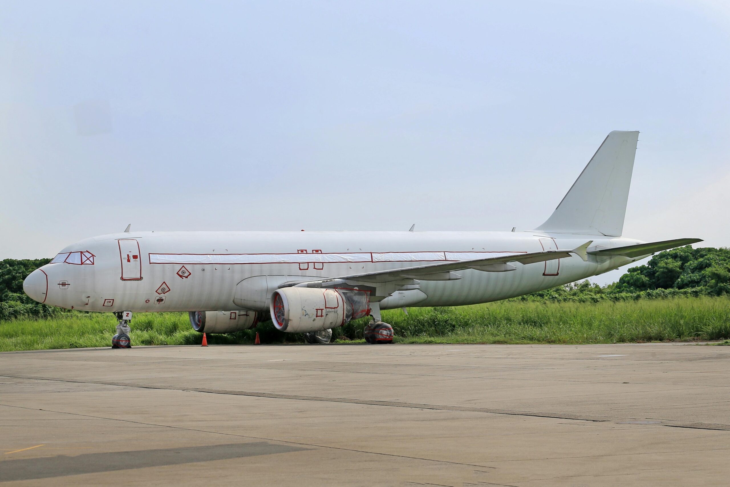 A white commercial airplane parked on a runway by lush green countryside during summer.