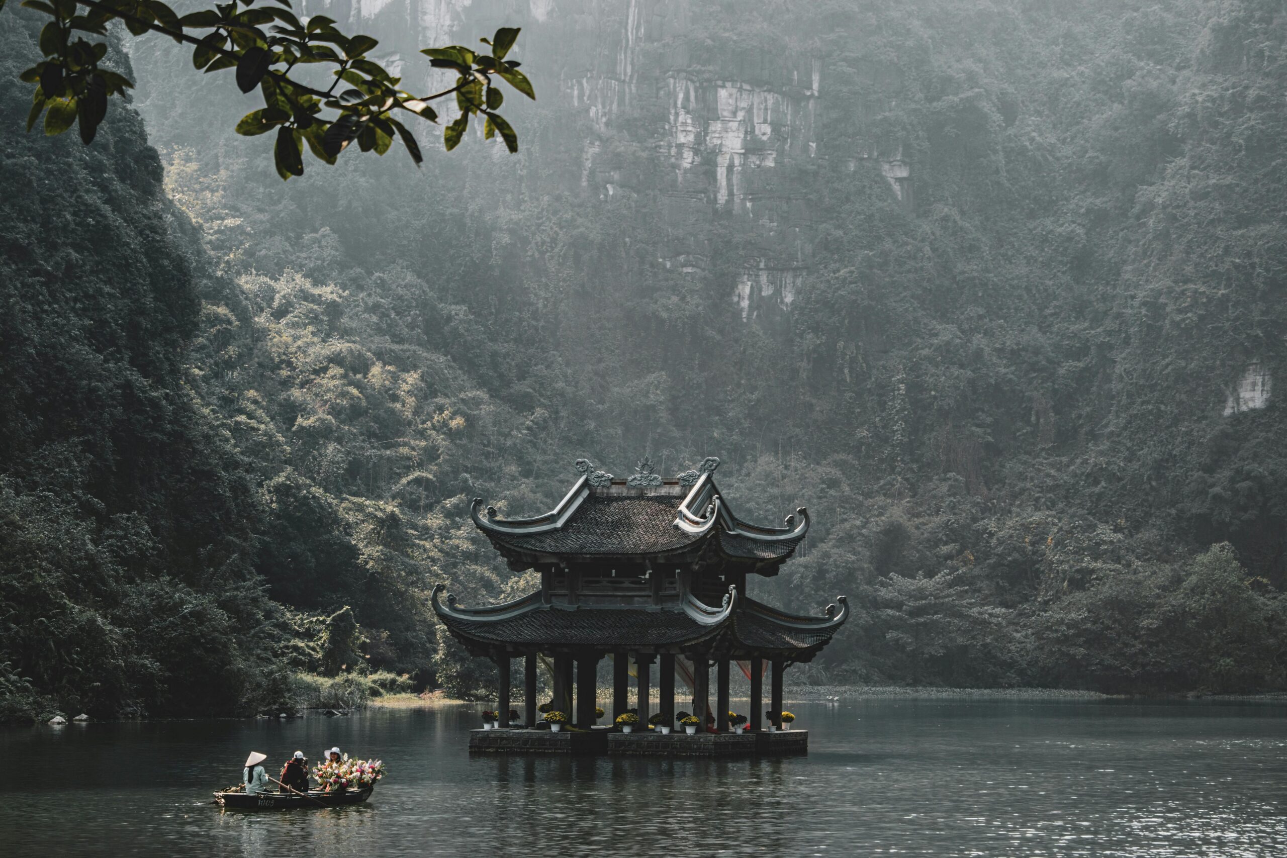 Serene scene of a traditional pagoda on the Tam Coc river in Ninh Bình, surrounded by lush greenery.