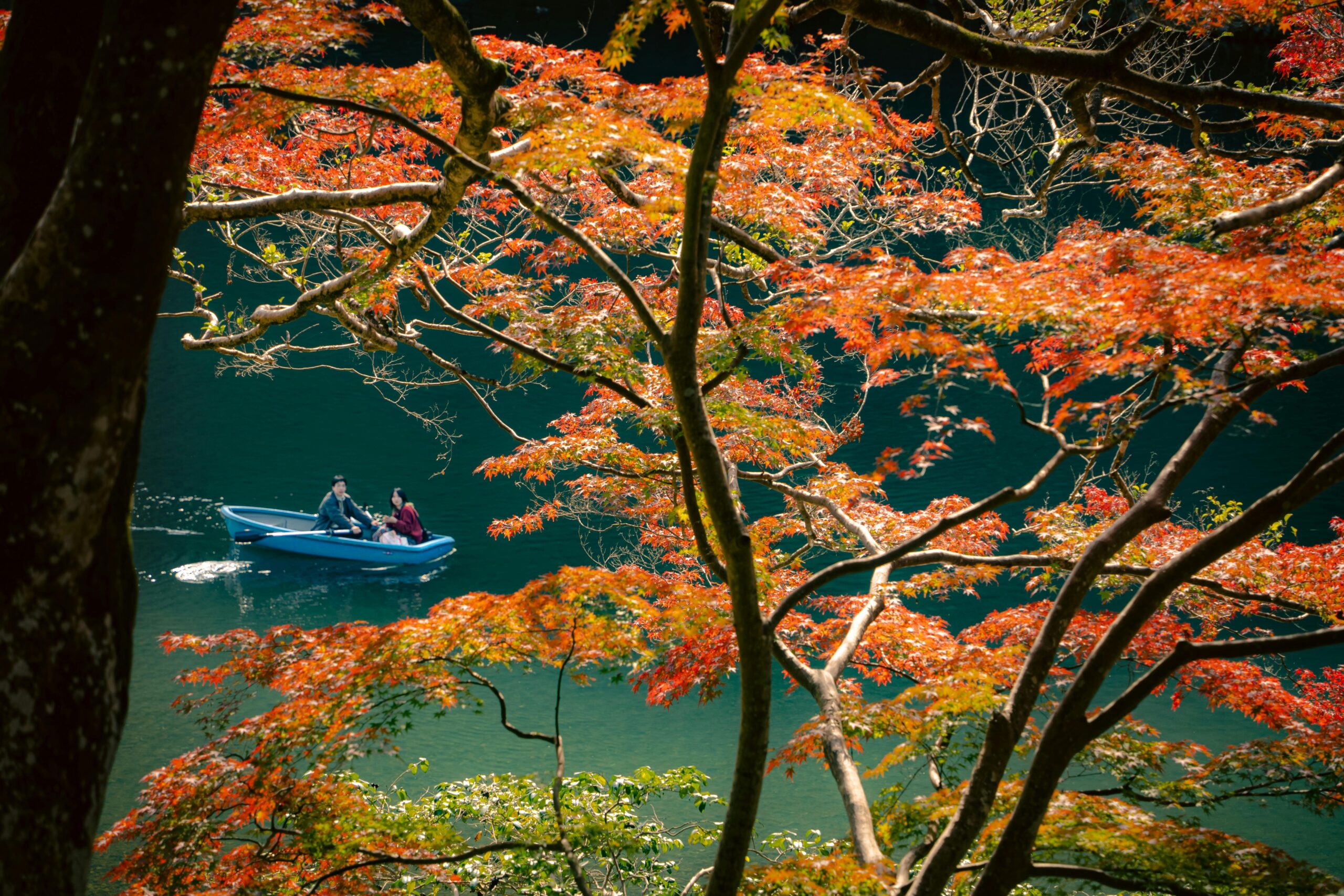 Scenic view of autumn foliage with people boating on a calm river in Kyoto, Japan.