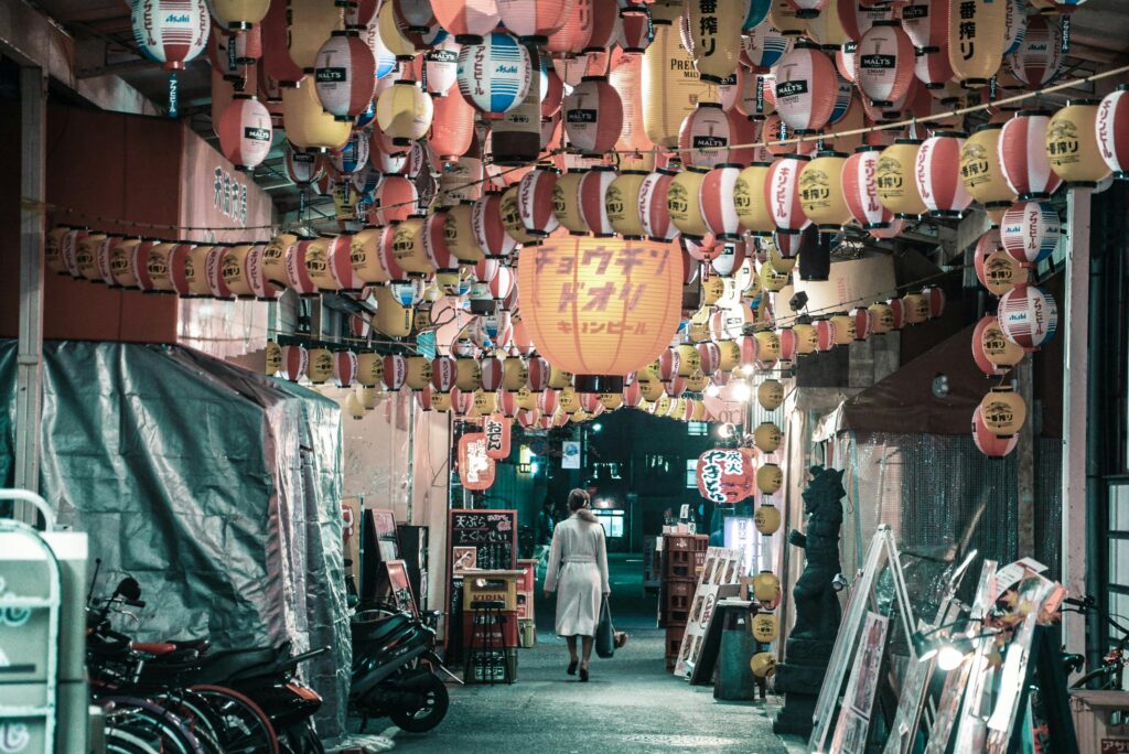 Vibrant nighttime market scene with hanging lanterns and a lone shopper.