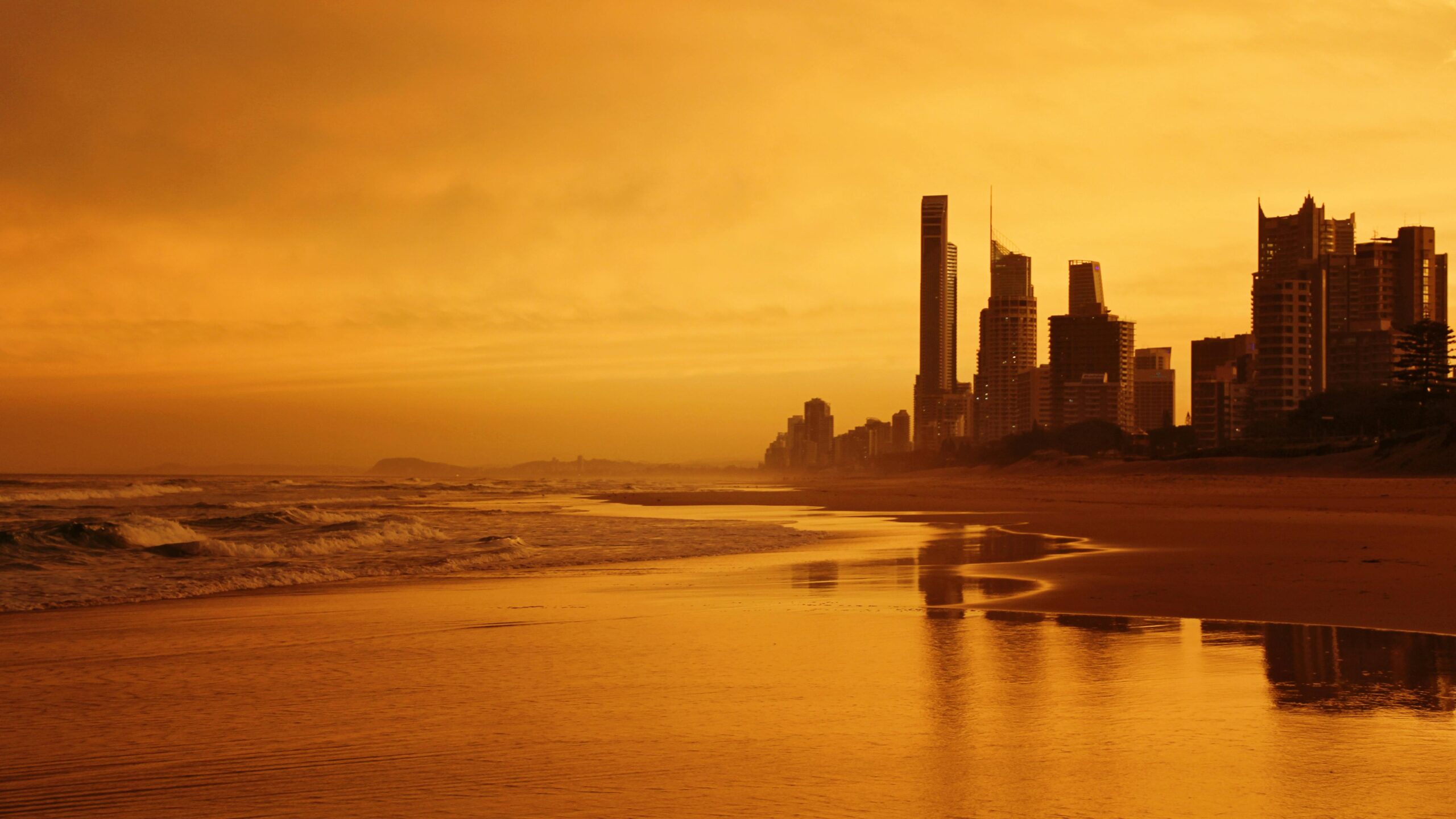 Dramatic sunset over Gold Coast skyline with golden reflections on the ocean waves.