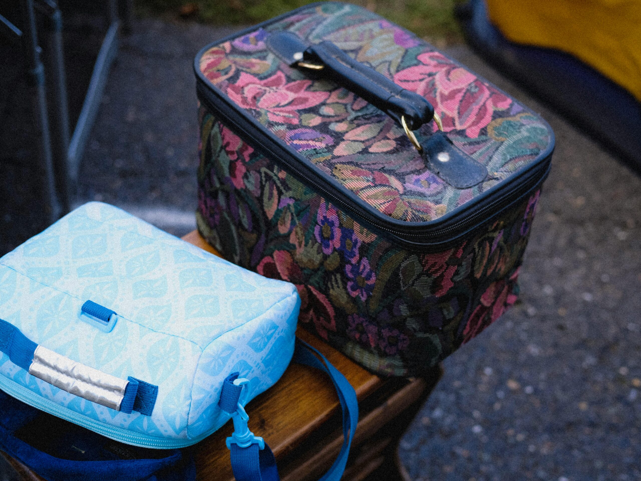 Two lunch bags, one with floral tapestry and one light blue, placed outdoors on a table.