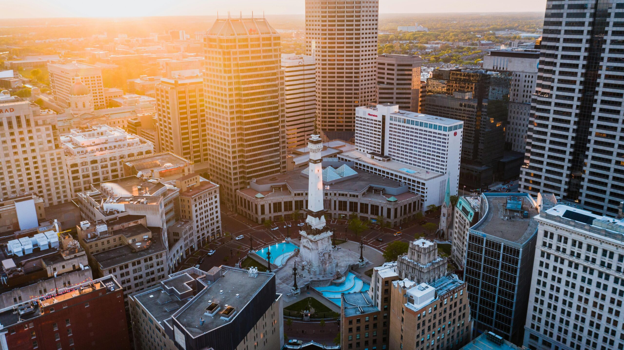 A scenic aerial view of downtown Indianapolis with prominent buildings and the Soldiers' and Sailors' Monument at dusk.