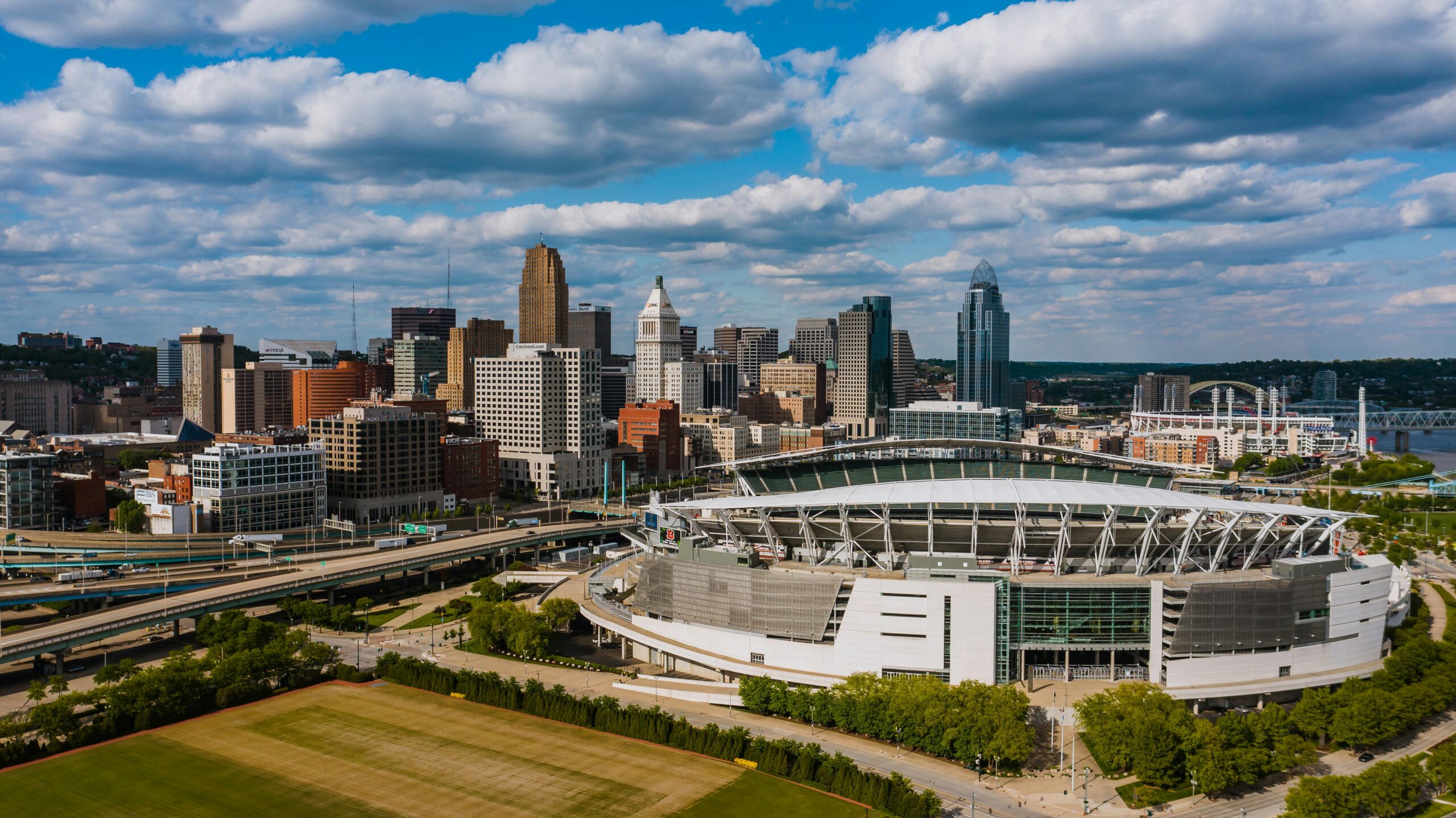 Exterior of modern Soldier Field in America surrounded by green trees and high multi storey office building next to junction and lawn
