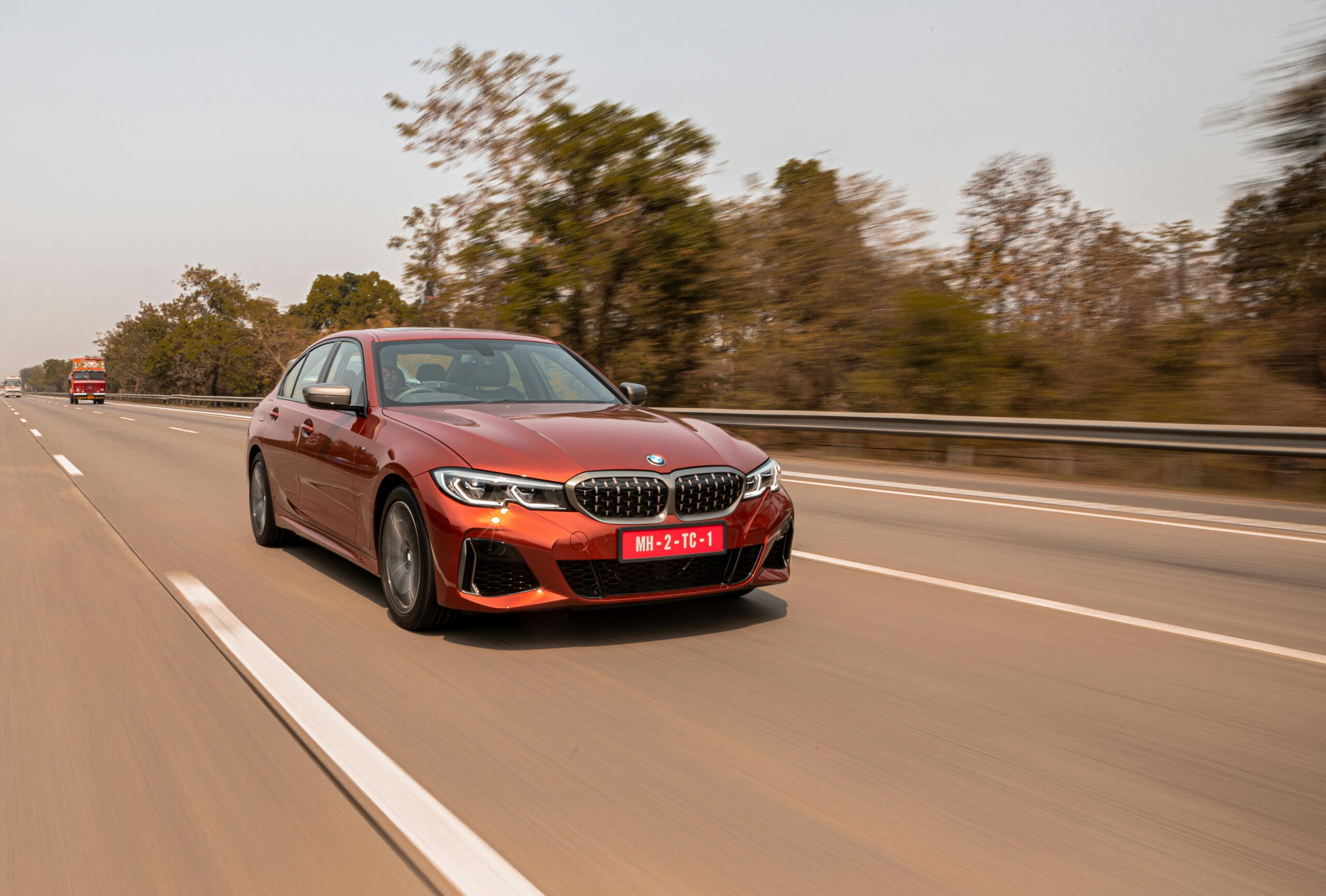 Red sedan driving on a highway in Mumbai, India, showcasing speed and motion on an urban road.