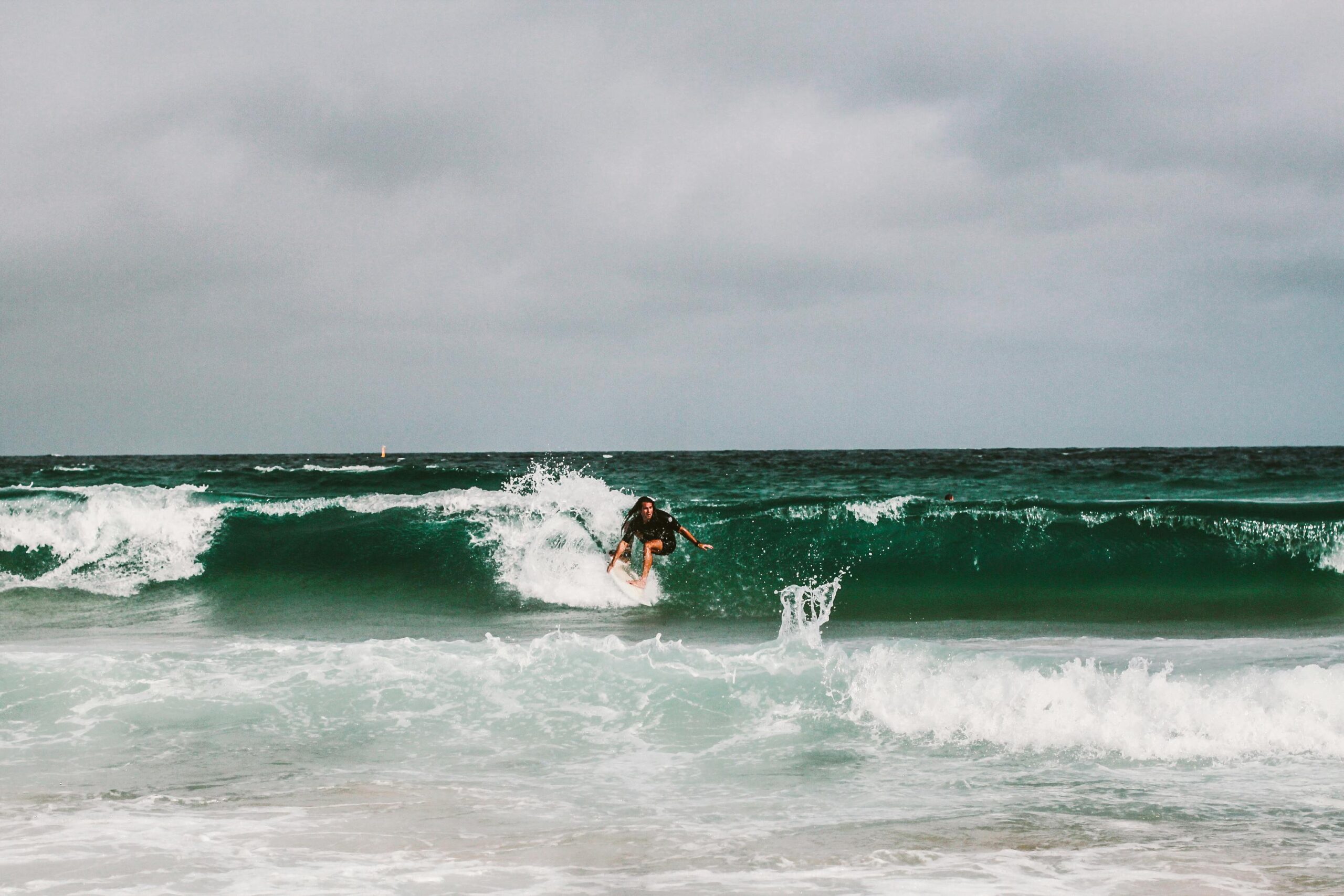 A surfer in action on the waves at Bondi Beach under overcast skies.